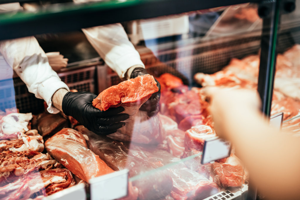 A butcher pulling raw meat from a meat display